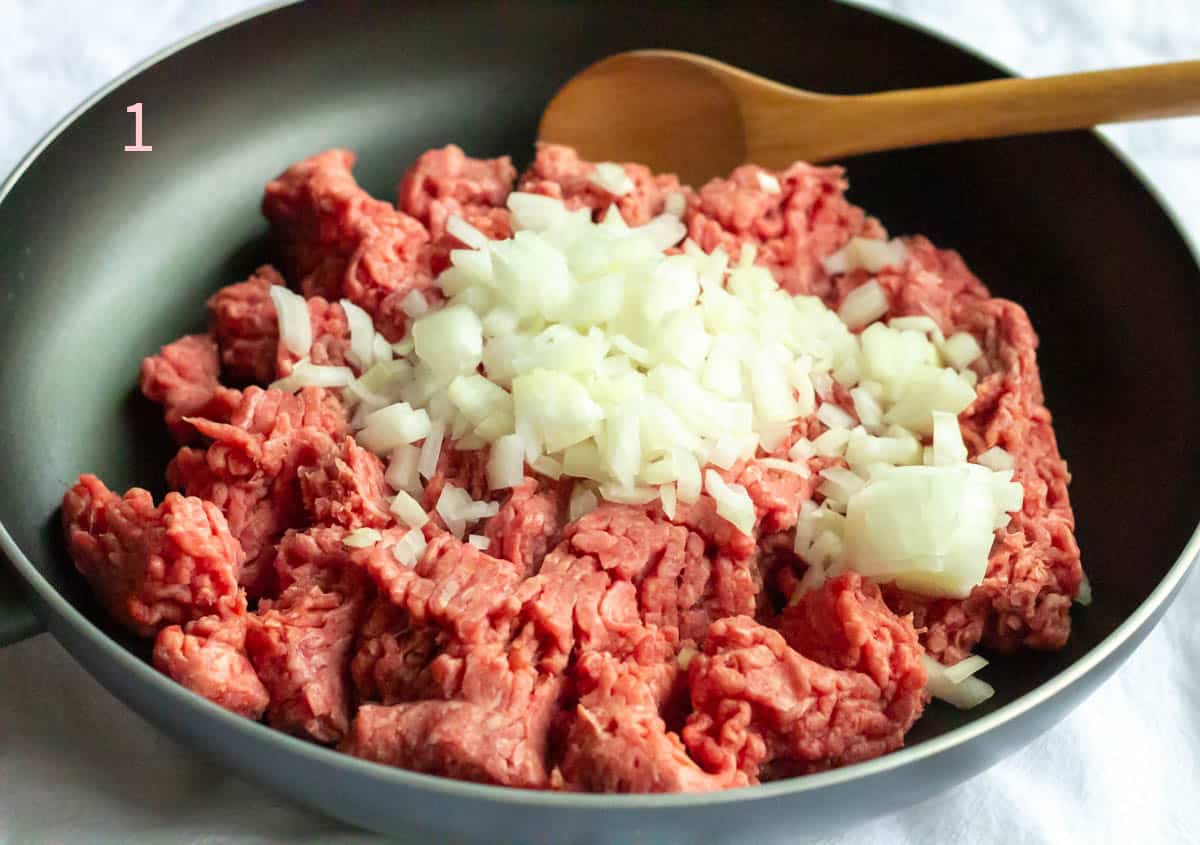 Raw ground beef and chopped onions in a large frying pan