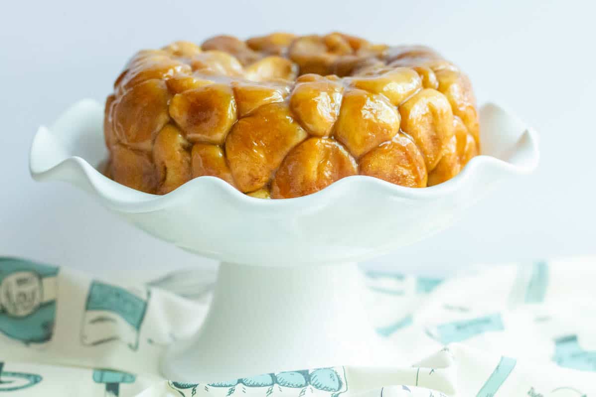 Monkey bread turned out onto a white cake plate with a blue and white towel surrounding the plate