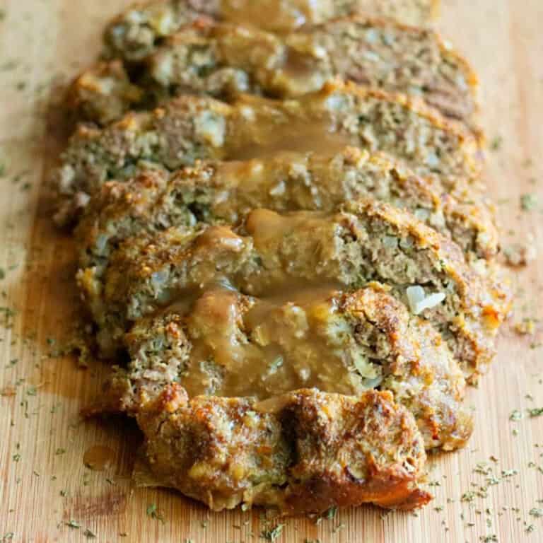 Sliced meatloaf with gravy on a cutting board