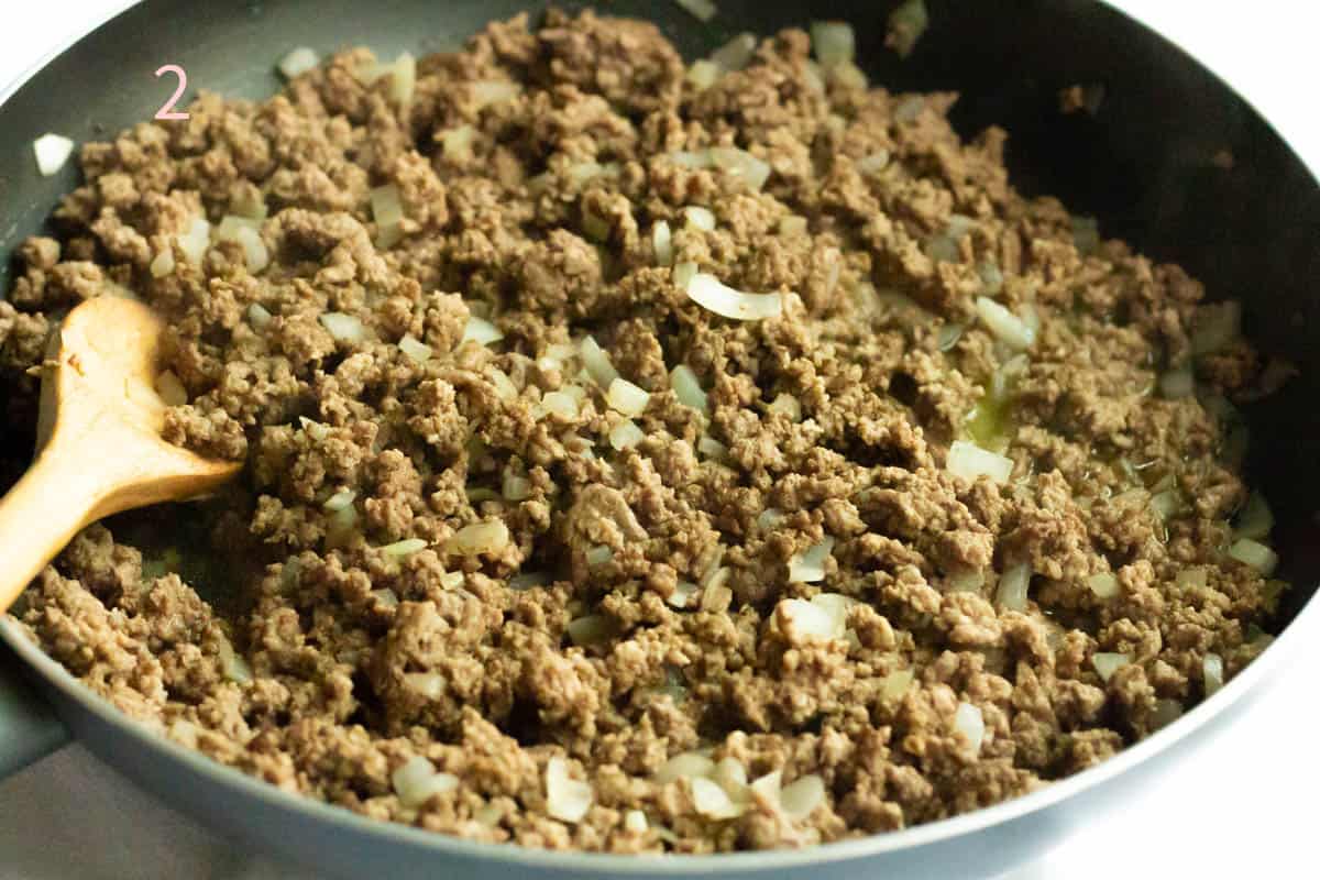 Browned ground beef and chopped onions in a large frying pan