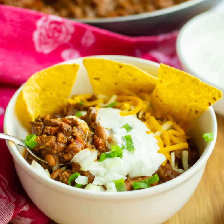 Chili in a white bowl with chips, sour cream and cheese