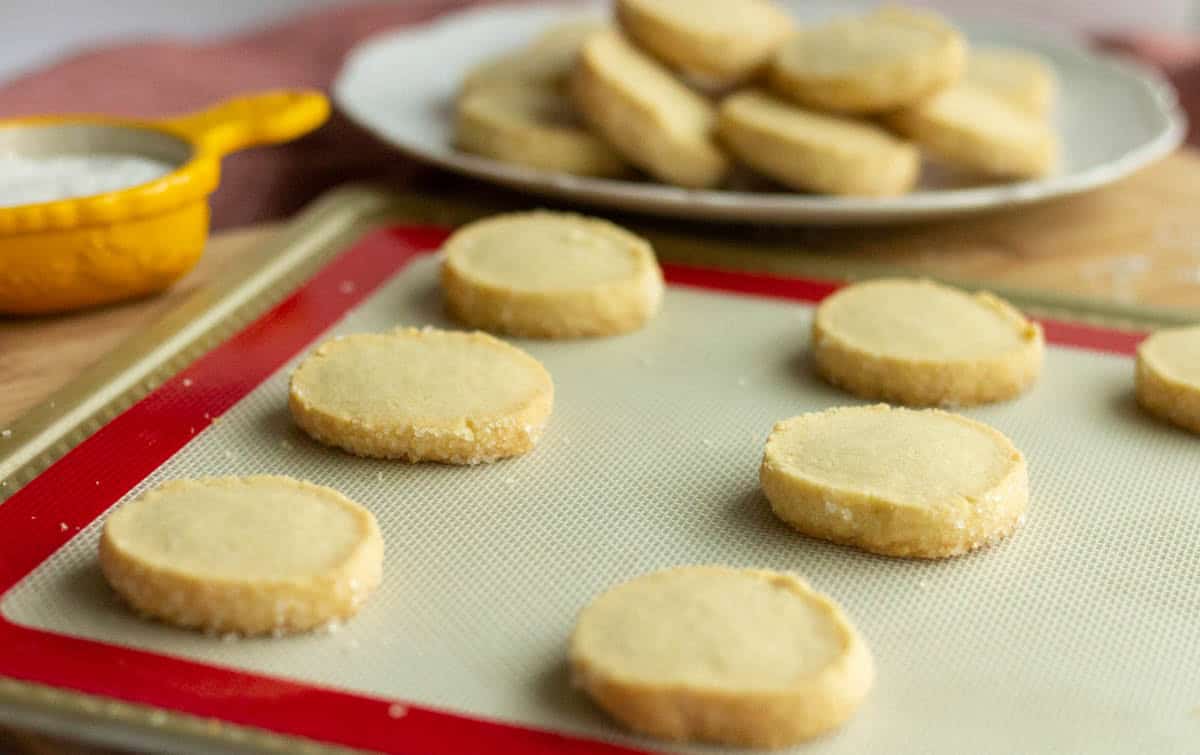 Old-Fashioned Butter Cookie Recipe | thewendthousekitchen.com Baked cookies on a Silpat on a cookie sheet with cookies on a plate in the background.