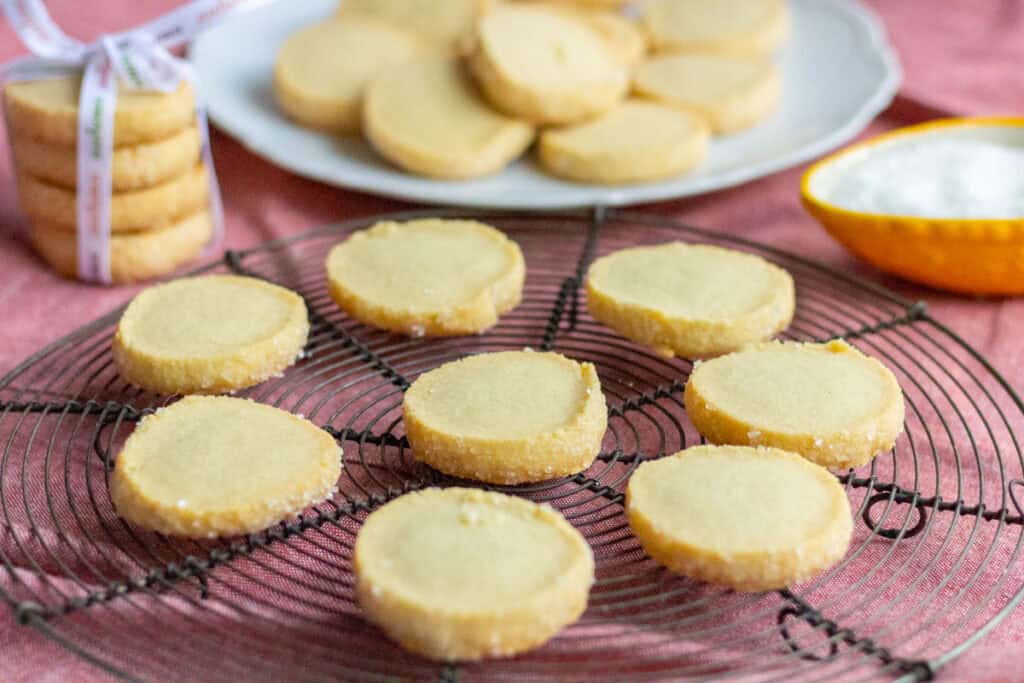 Old-Fashioned Butter Cookie Recipe | thewendthousekitchen.com Baked cookies on a black wire grid with cookies on a plate in the background.