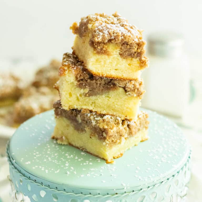 Squares of crumb cake stacked on a small mint green cake pedestal