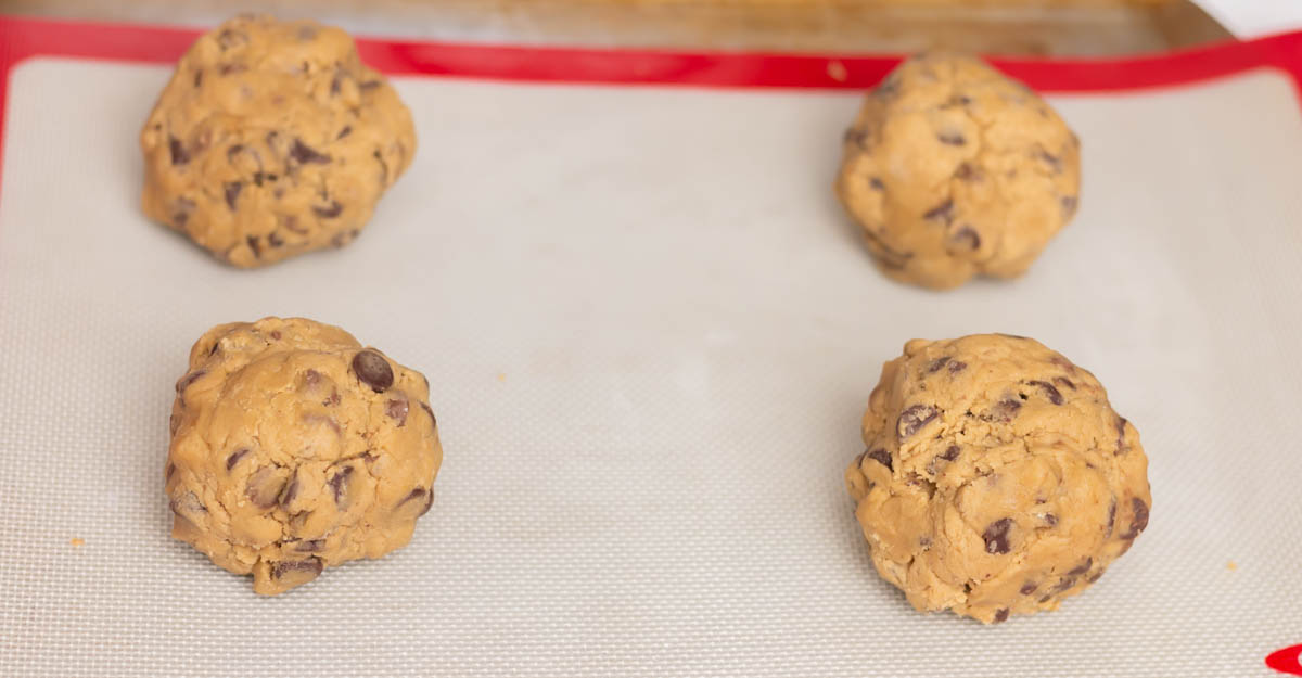 Four balls of chocolate chip cookie dough on a Silpat on a cookie sheet