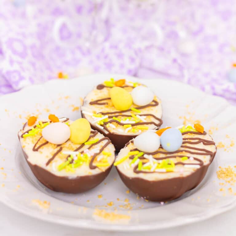 Three Easter Egg Cheesecakes on a white plate with a white towel with lavender flowers in the background