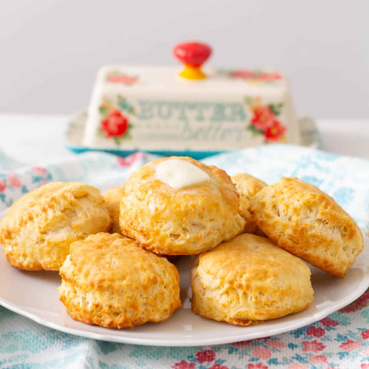 Buttermilk biscuits stacked on a white plate with a butter dish in the background