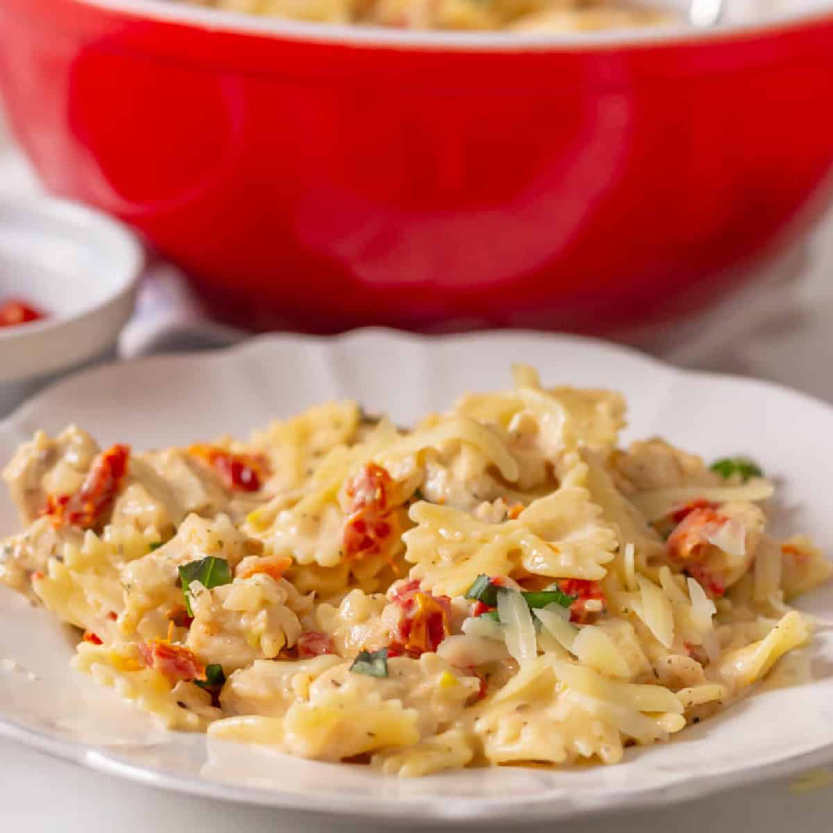 Marry Me Pasta on a white plate with a red serving bowl in the background