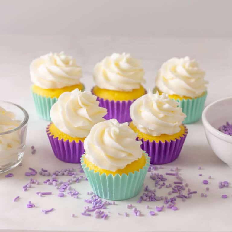 Frosted cupcakes in light aqua and purple cupcake liners with purple sprinkles on the counter