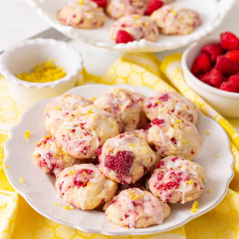 Lemon raspberry cookies on a white plate with more cookies in the background on a white cake pedestal