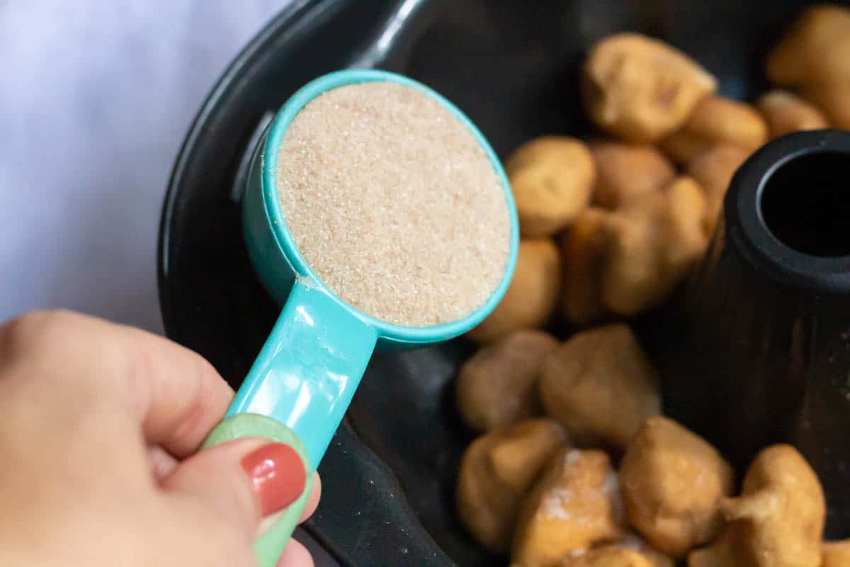 Pouring cinnamon sugar onto cut up rolls inside of a dark Bundt pan