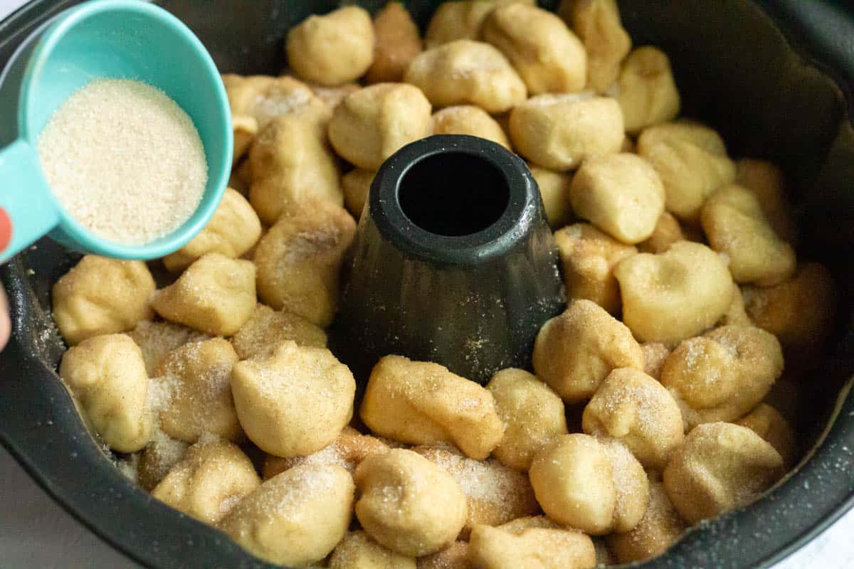 Pouring cinnamon sugar onto cut up rolls inside of a dark Bundt pan