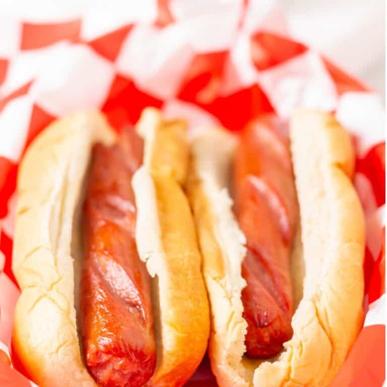Two air fried hot dogs in buns in red and white check parchment paper
