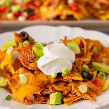Instant Pot Chicken Nachos on a white plate with a pan of nachos in the background