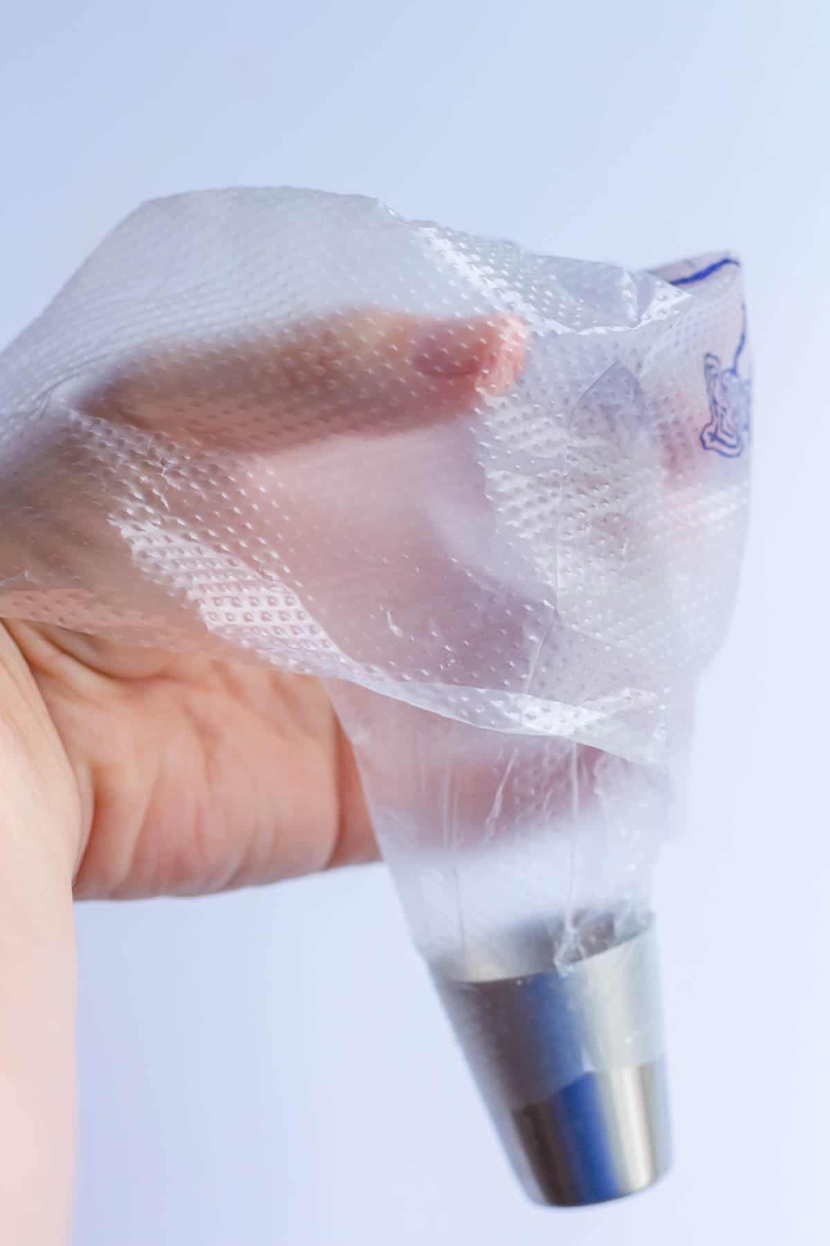 A piping bag fitted with a piping tip and the bag is folded down halfway onto a hand