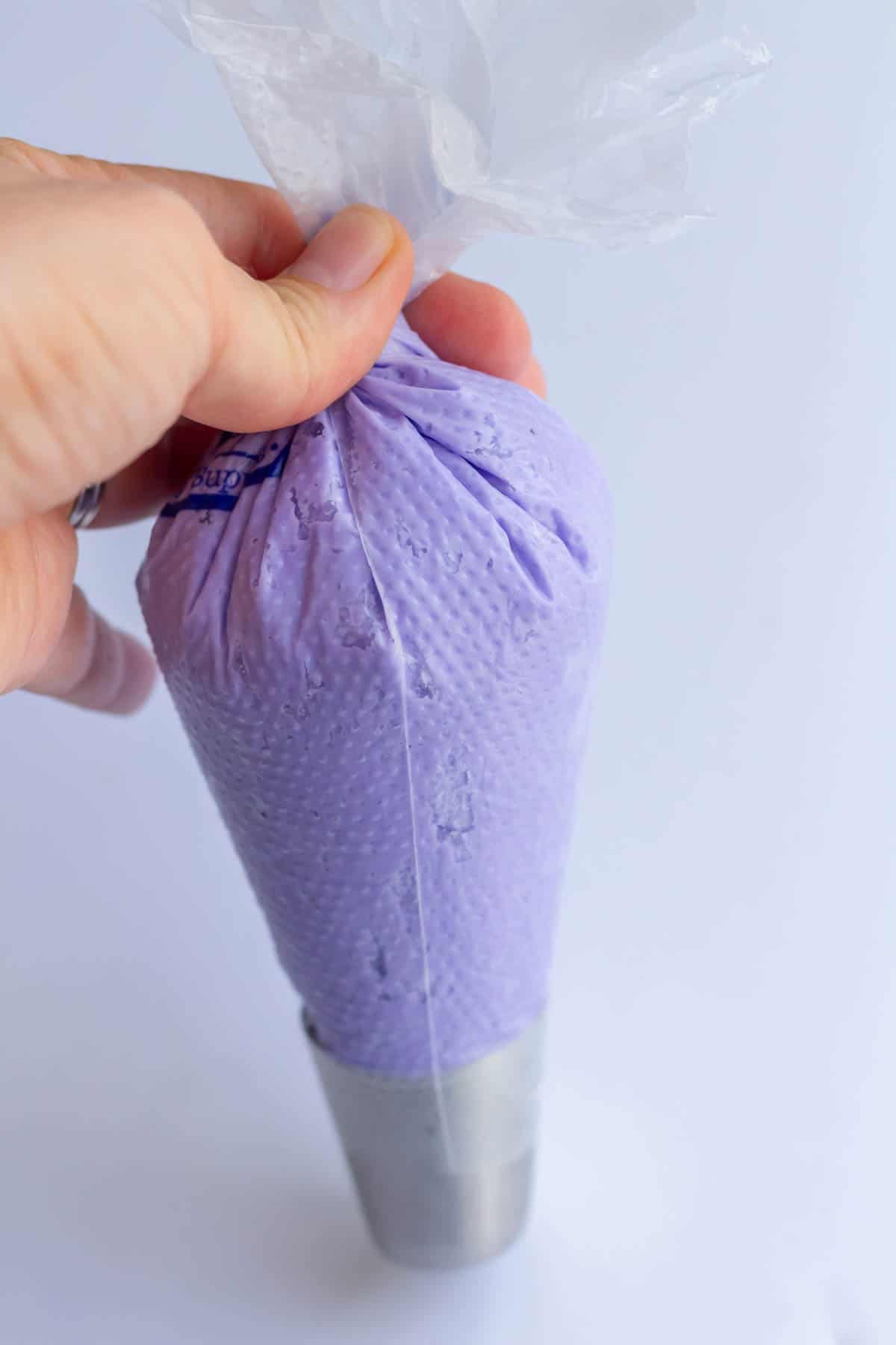A 16-inch piping bag filled halfway with lavender buttercream, fitted with a piping tip and the top of the bag is twisted closed