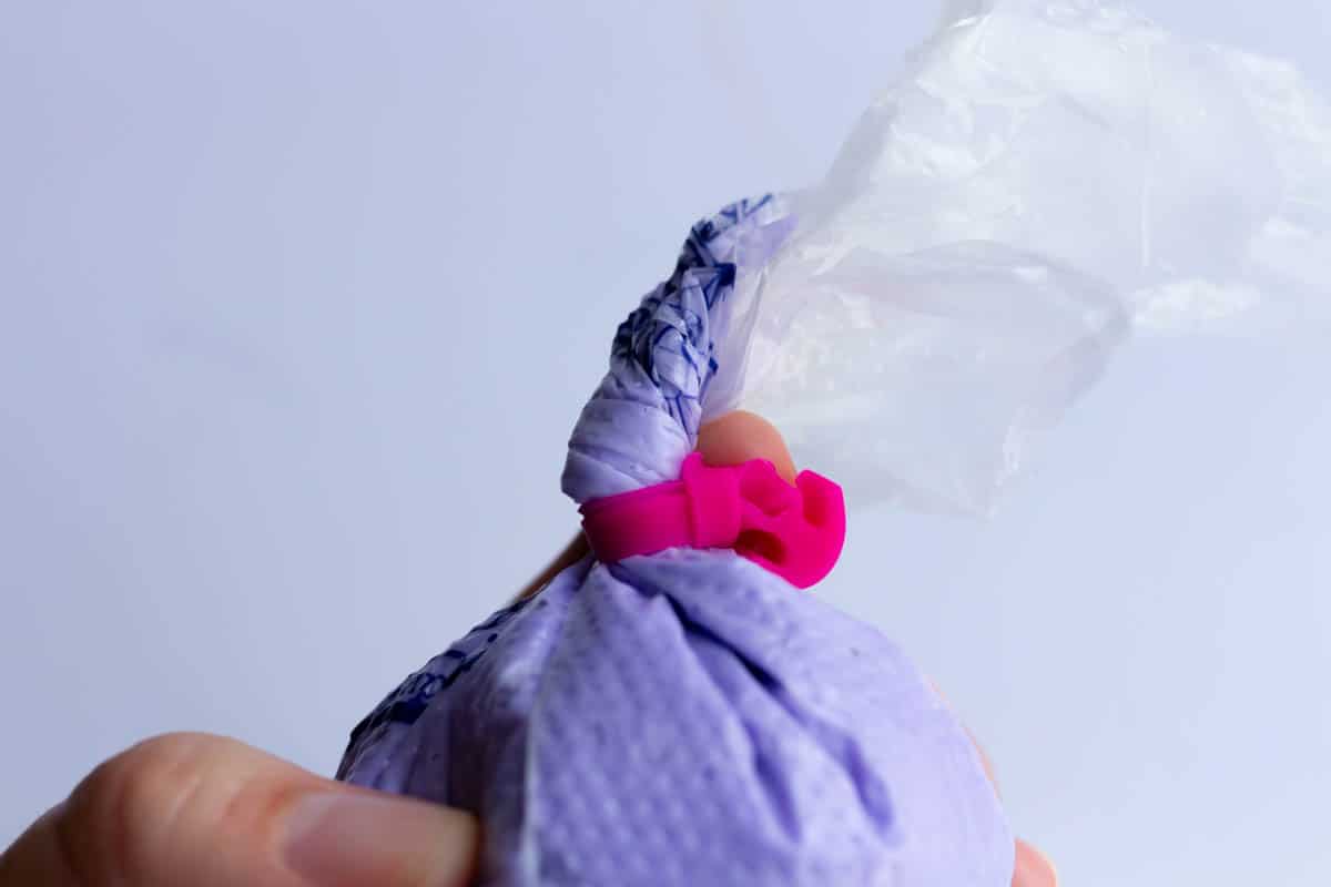 A piping bag filled with lavender buttercream and fastened with a piping bag tie