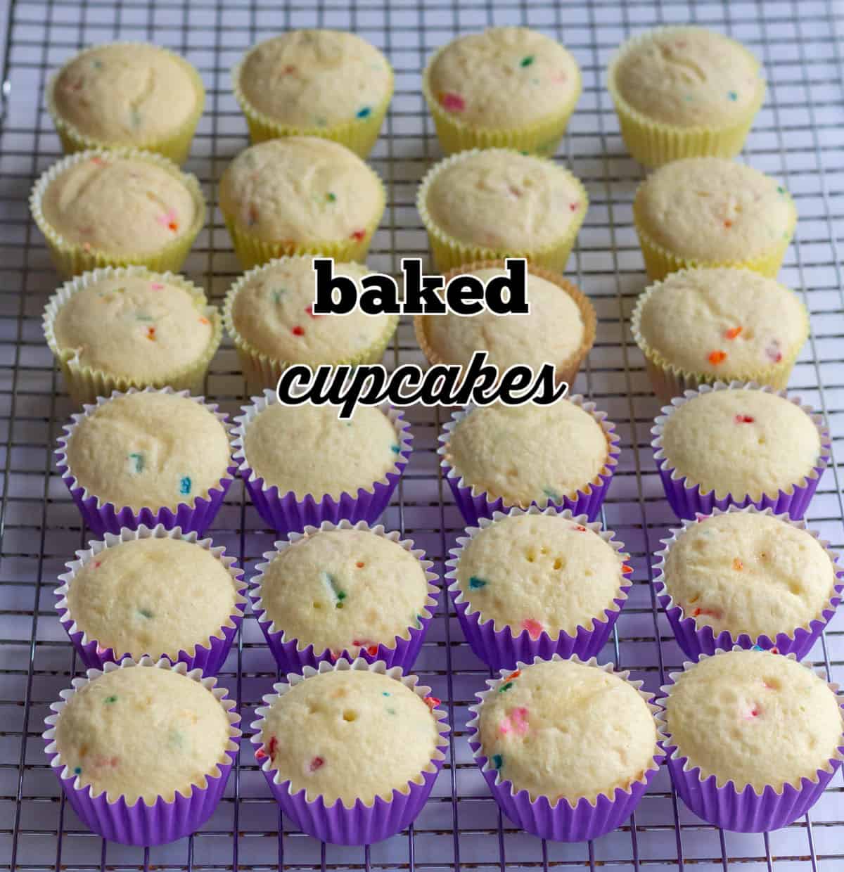Baked, undecorated cupcakes in yellow and purple cupcake liners on a wire grid and labeled