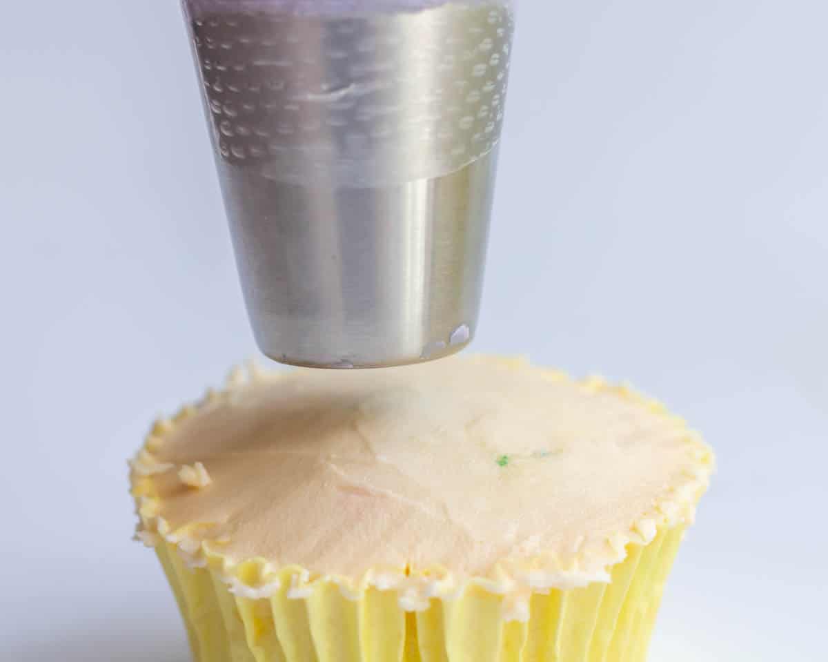 Holding a piping bag over an iced cupcake so the tip is not touching the cupcake