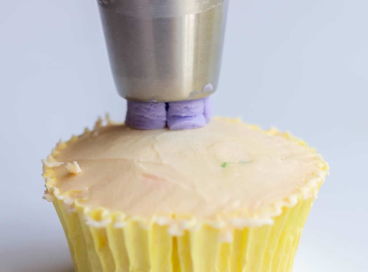 Piping a lavender buttercream flower onto an iced cupcake