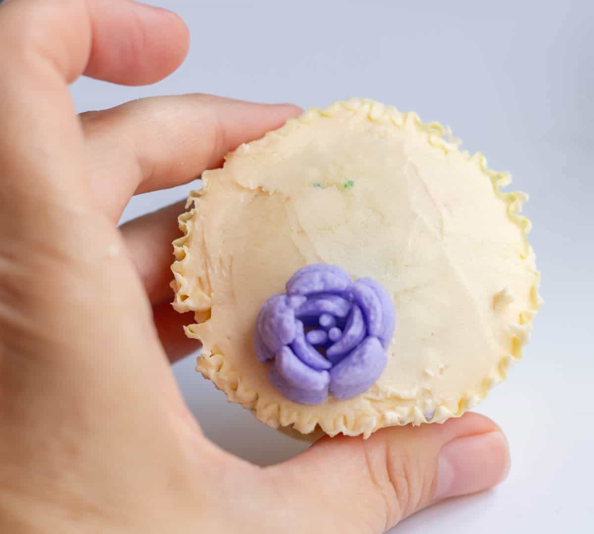A lavender buttercream flower on an iced cupcake