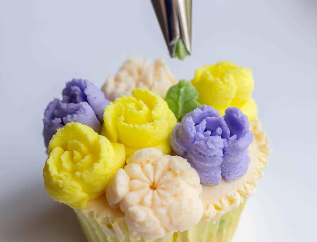 Holding a #352 piping tip over a green leaf that was just piped in between buttercream flowers on a cupcake