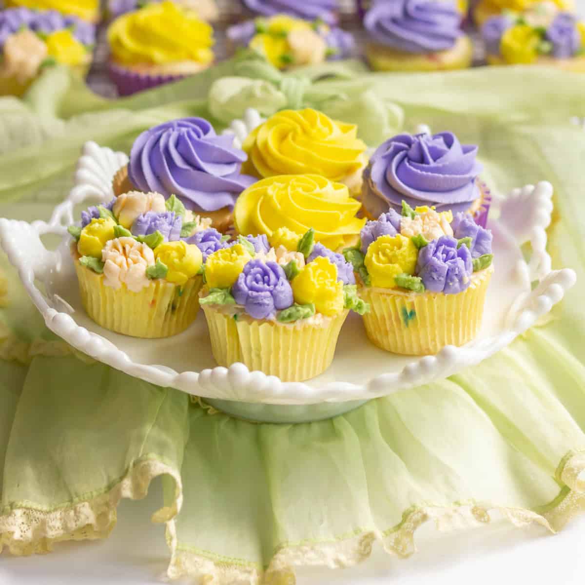 Lavender and yellow cupcakes on a white cake pedestal with cupcakes in the back