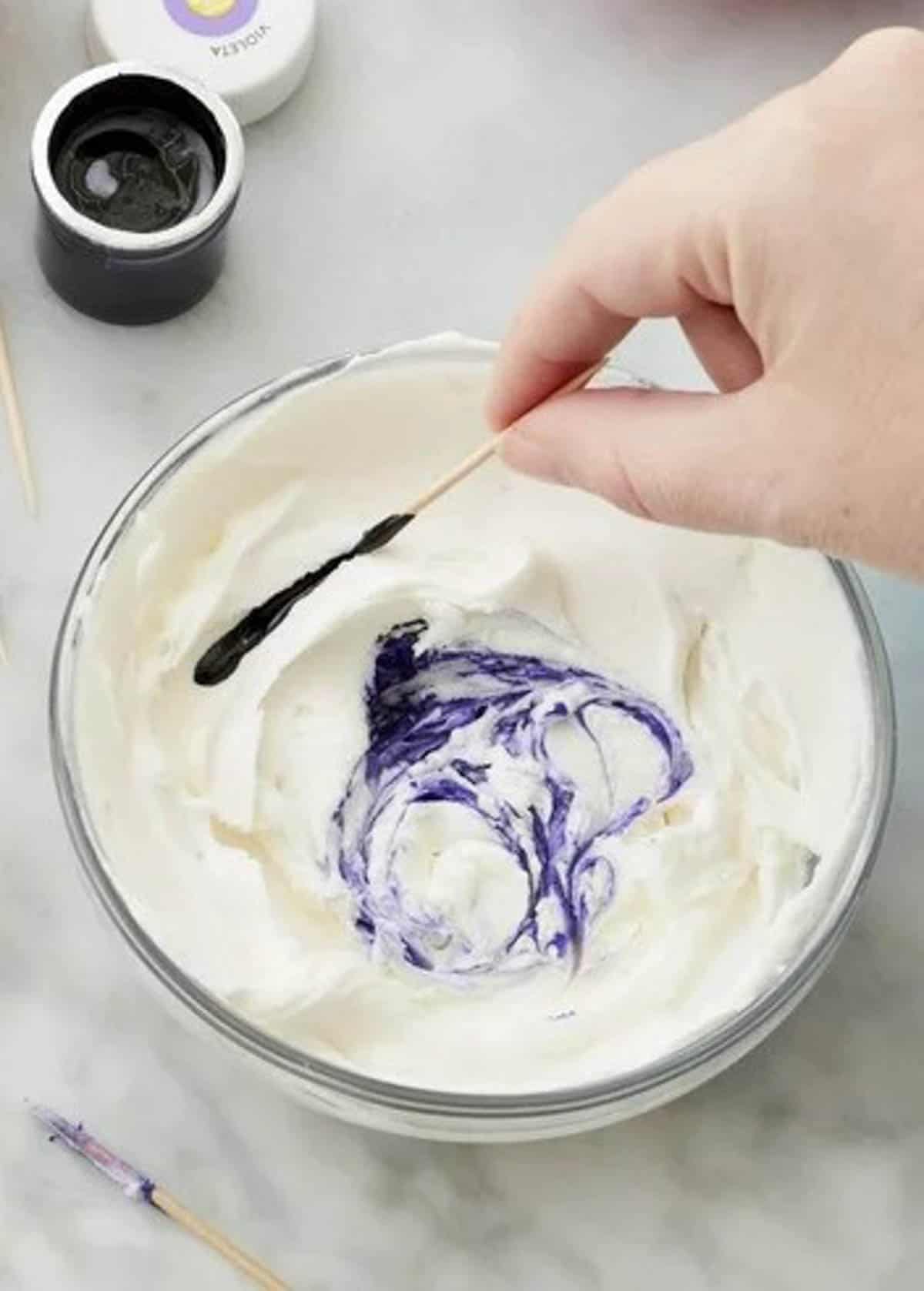 Coloring buttercream lavender in a bowl with a toothpick and gel food color