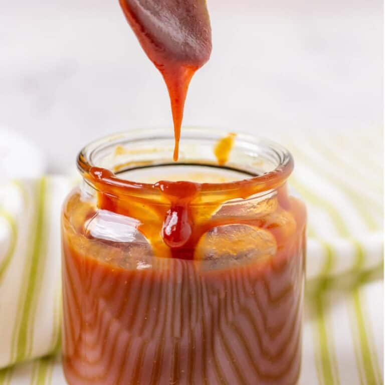 BBQ sauce in a glass jar with a spoon dripping with sauce