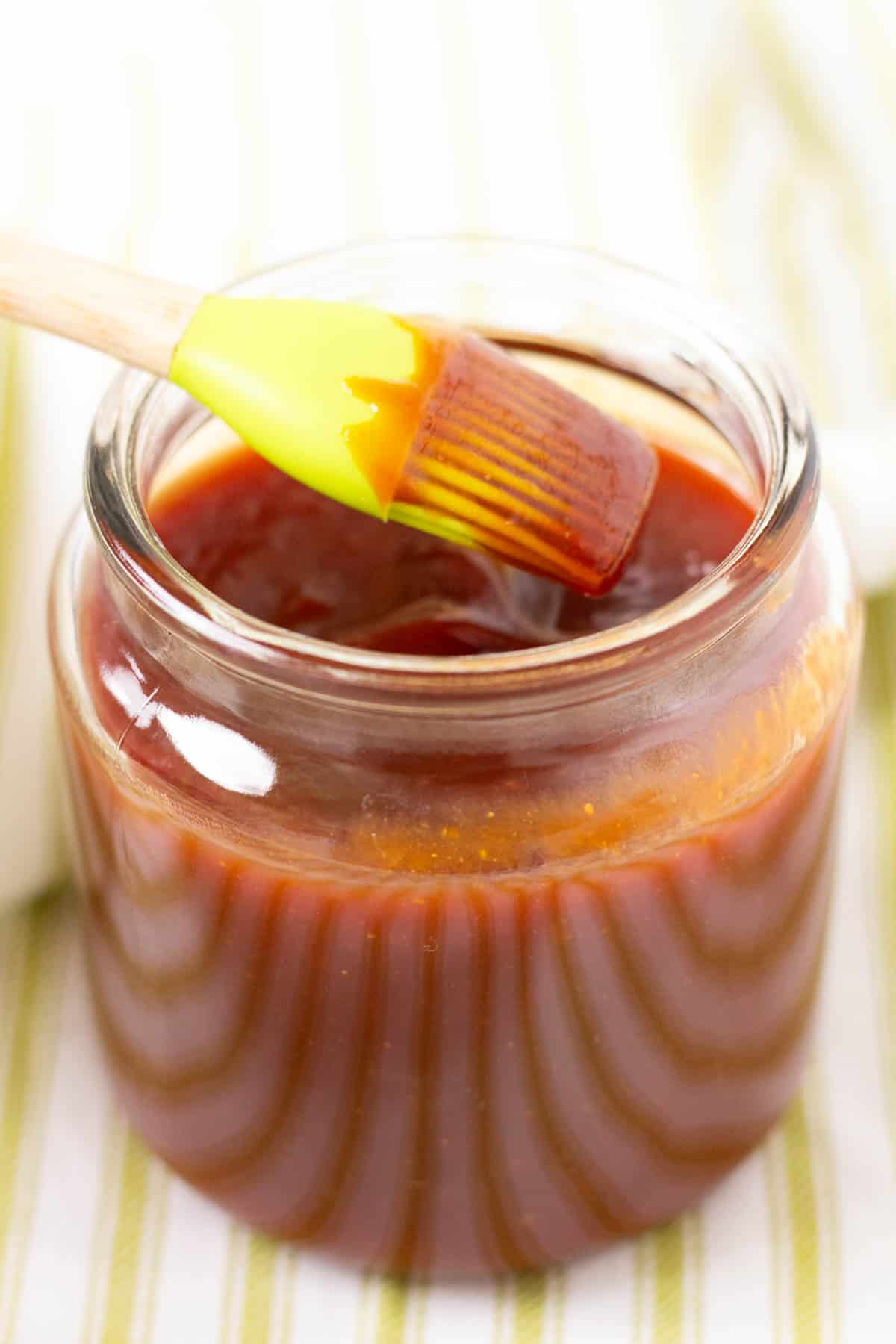 BBQ sauce in a glass jar with a green basting brush