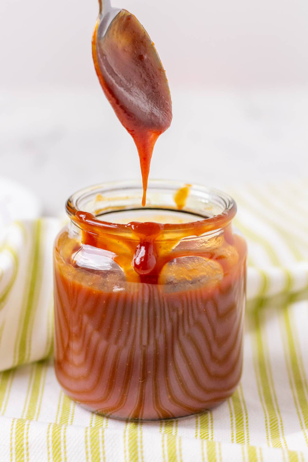 Barbecue sauce dripping off of a spoon and into a glass jar 