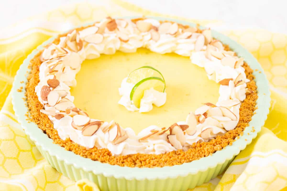 Key Lime Pie in a green pie plate with whipped cream and almonds