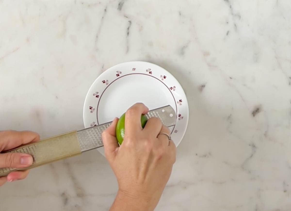 Zesting a lime with a zester over a white and red plate