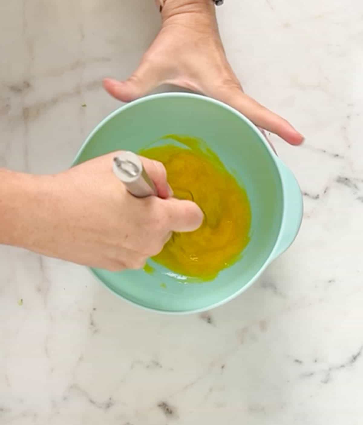 Beating egg yolks with a whisk in a medium aqua mixing bowl