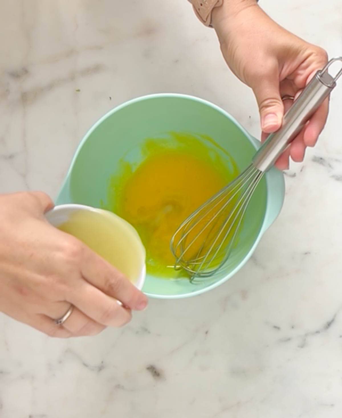Pouring lime juice into egg yolks in a medium aqua mixing bowl