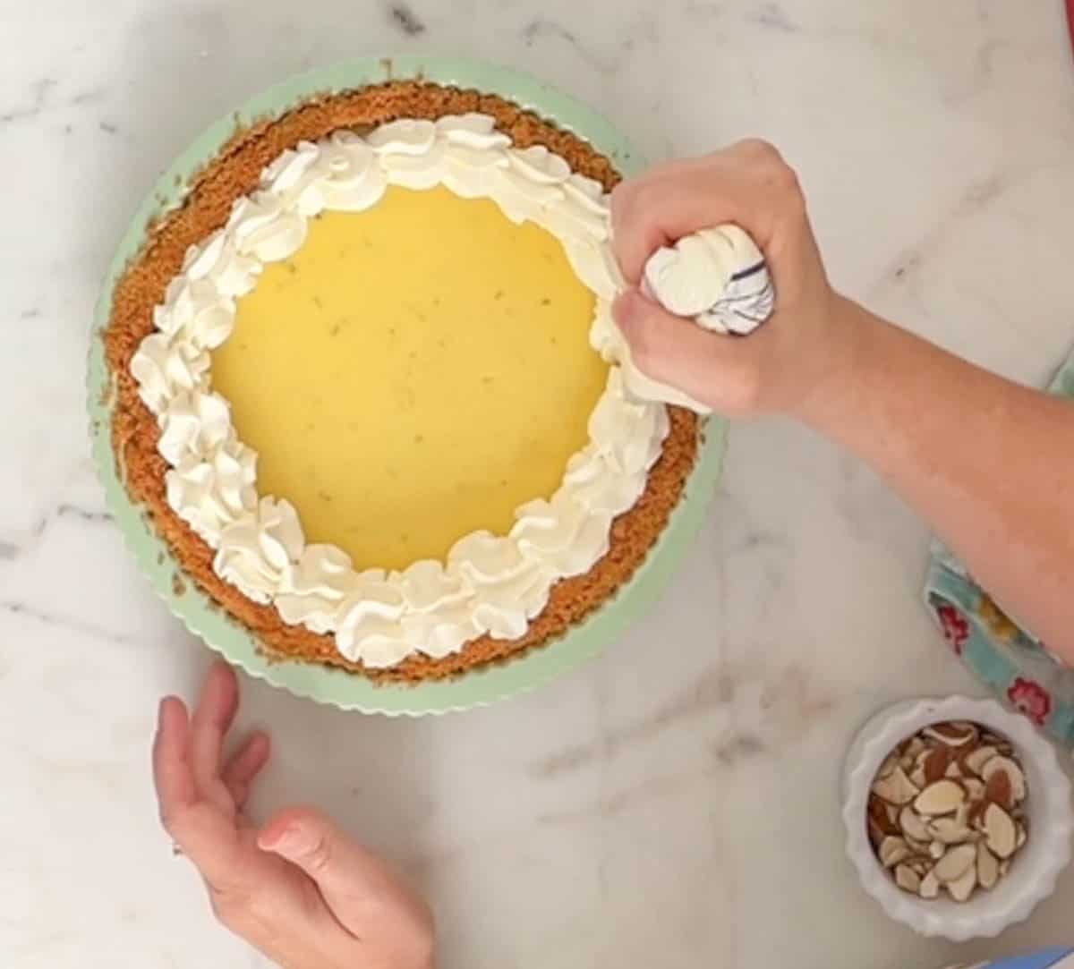 Piping a whipped cream shell border onto a key lime pie in a green pie plate