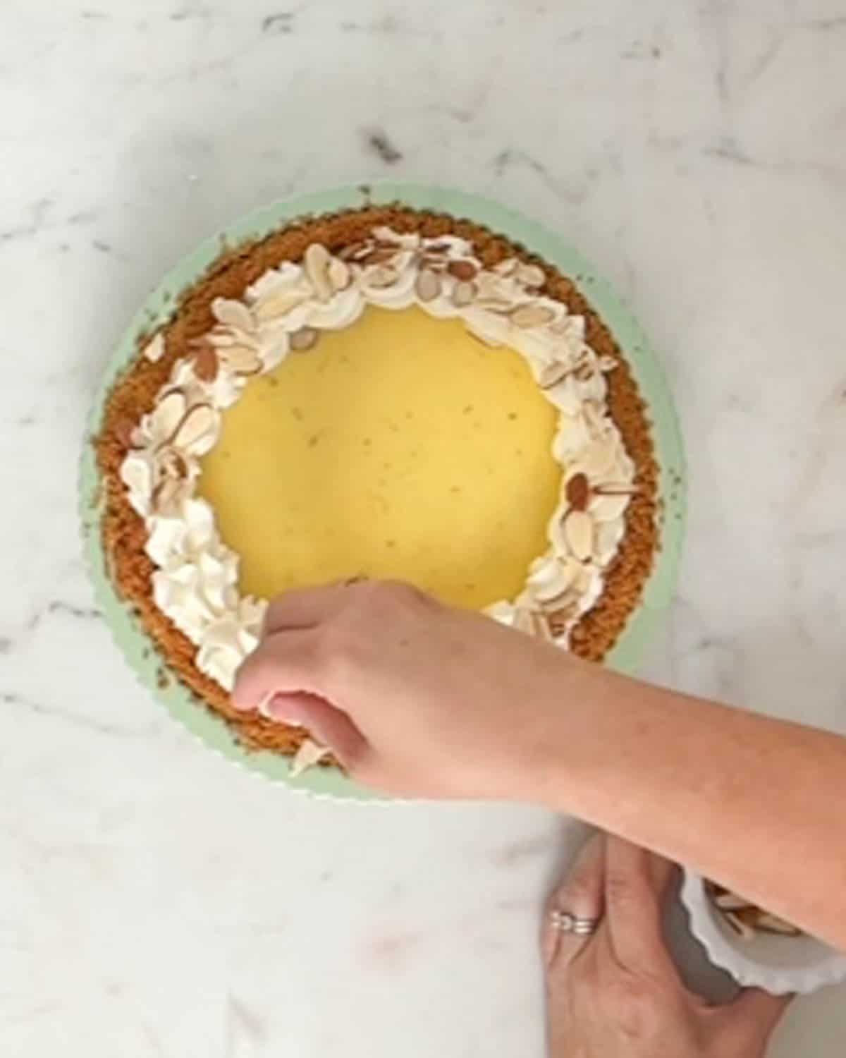 Sprinkling slivered almonds onto a whipped cream shell border on a key lime pie