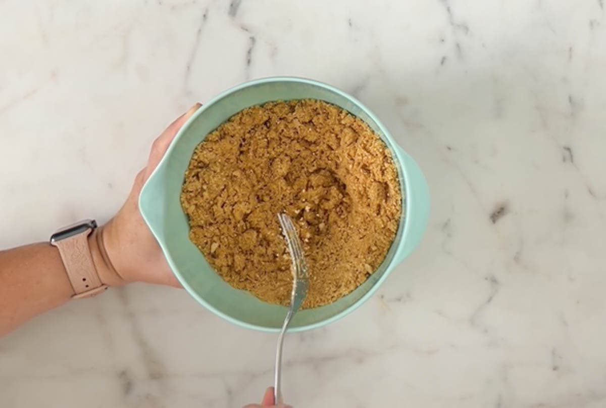 Melted butter combined with graham cracker crumbs and sugar in a medium aqua mixing bowl
