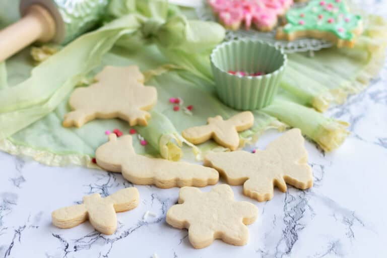 Baked cookie cutouts with a green apron in the background and a cup of sprinkles.