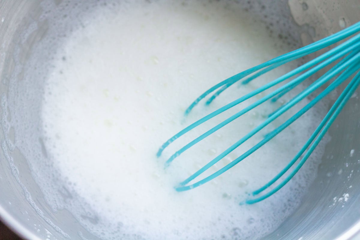 Royal Icing Recipe with Meringue Powder | thewendthousekitchen.com Water mixed with meringue powder in the bowl of a stand mixer with an aqua whisk.