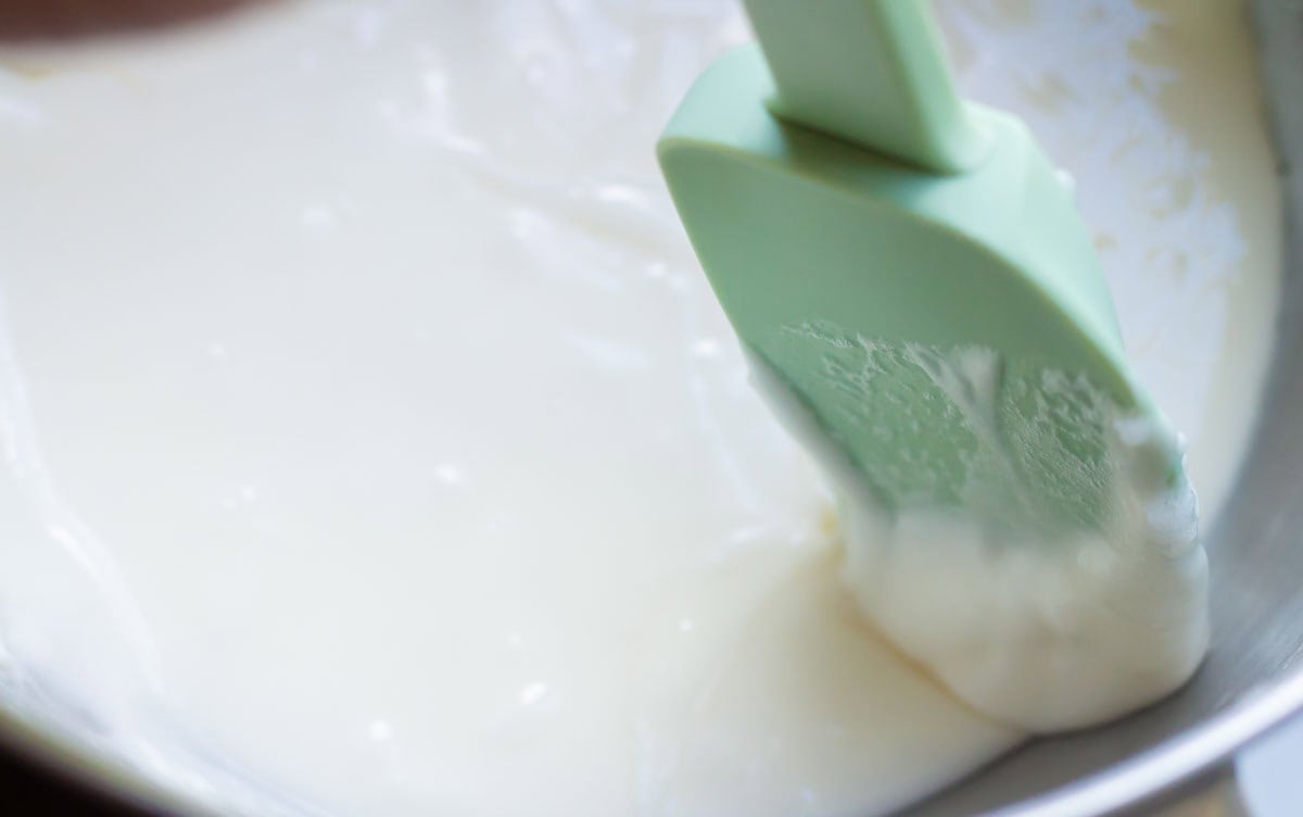 Royal Icing Recipe with Meringue Powder | thewendthousekitchen.com A green rubber spatula scraping down the sides of a bowl of a stand mixer with royal icing.