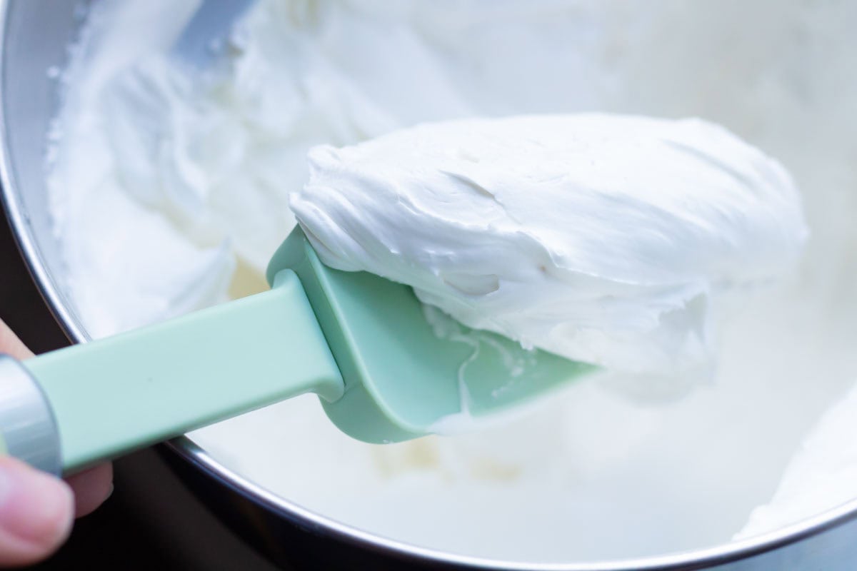 Royal Icing Recipe with Meringue Powder | thewendthousekitchen.com Royal icing on a green rubber spatula over the bowl of a stand mixer.