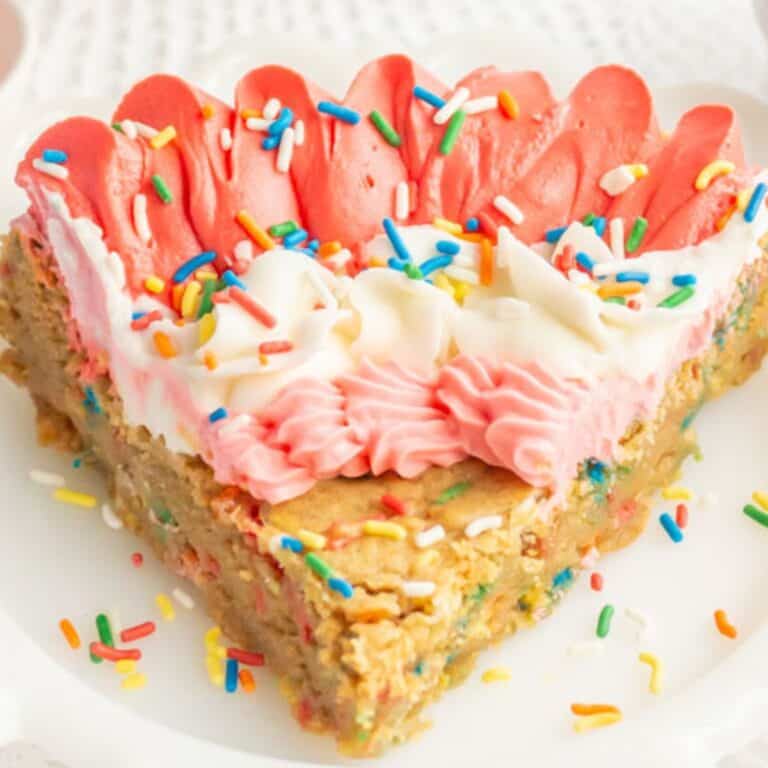 A piece of funfetti cookie cake frosted with pink and white frosting on a white plate.
