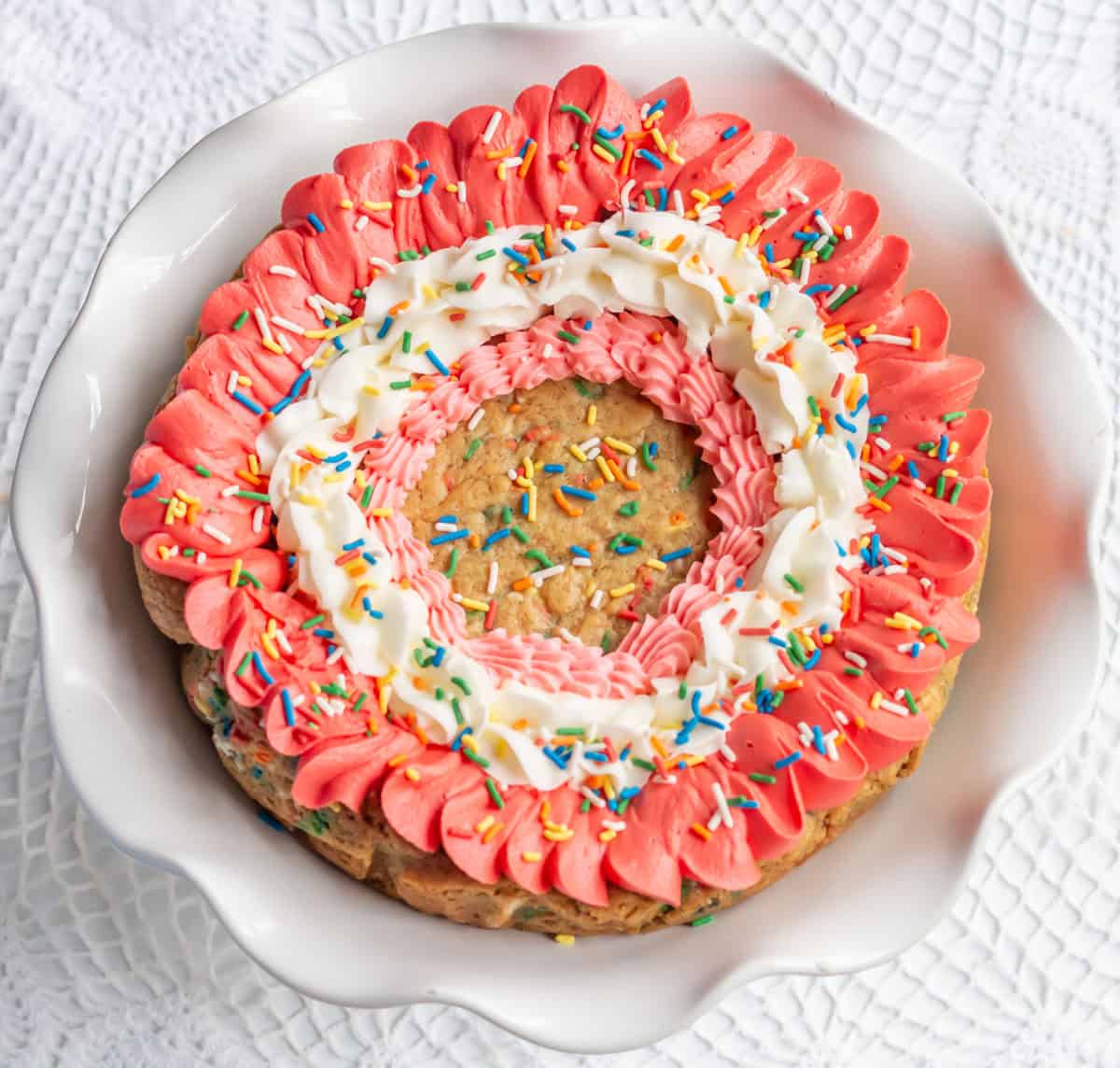 Decorated cookie cake with pink and white buttercream frosting and topped with rainbow sprinkles.