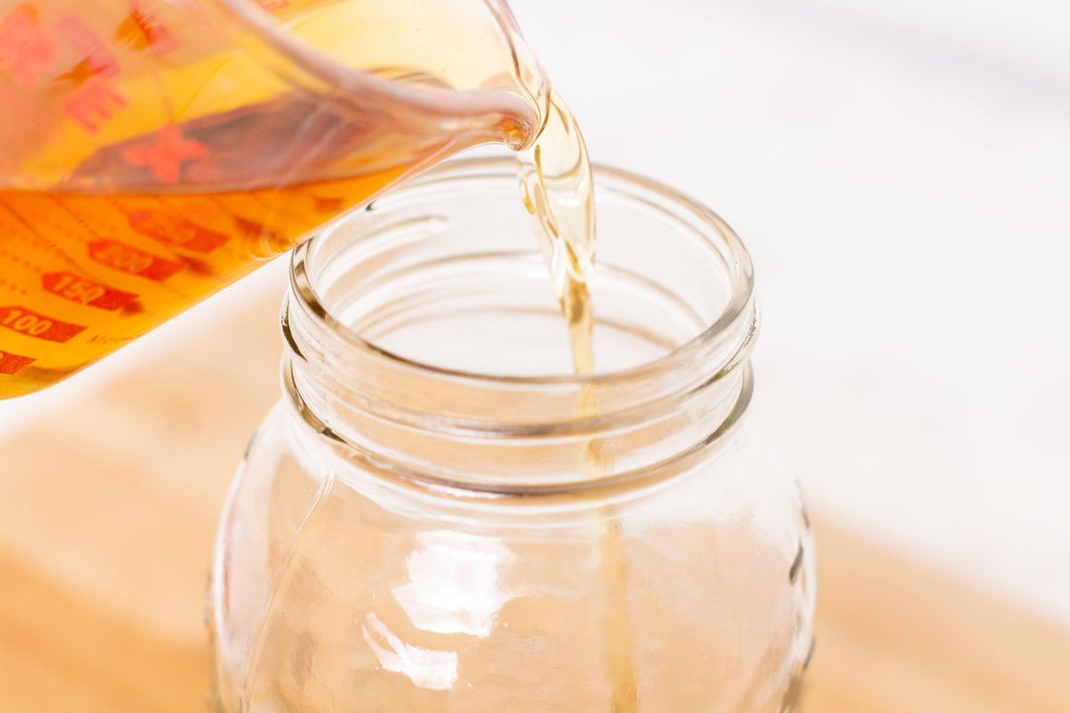 Easy Bourbon Vanilla Extract | thewendthousekitchen.com Pouring bourbon into a glass Mason jar.