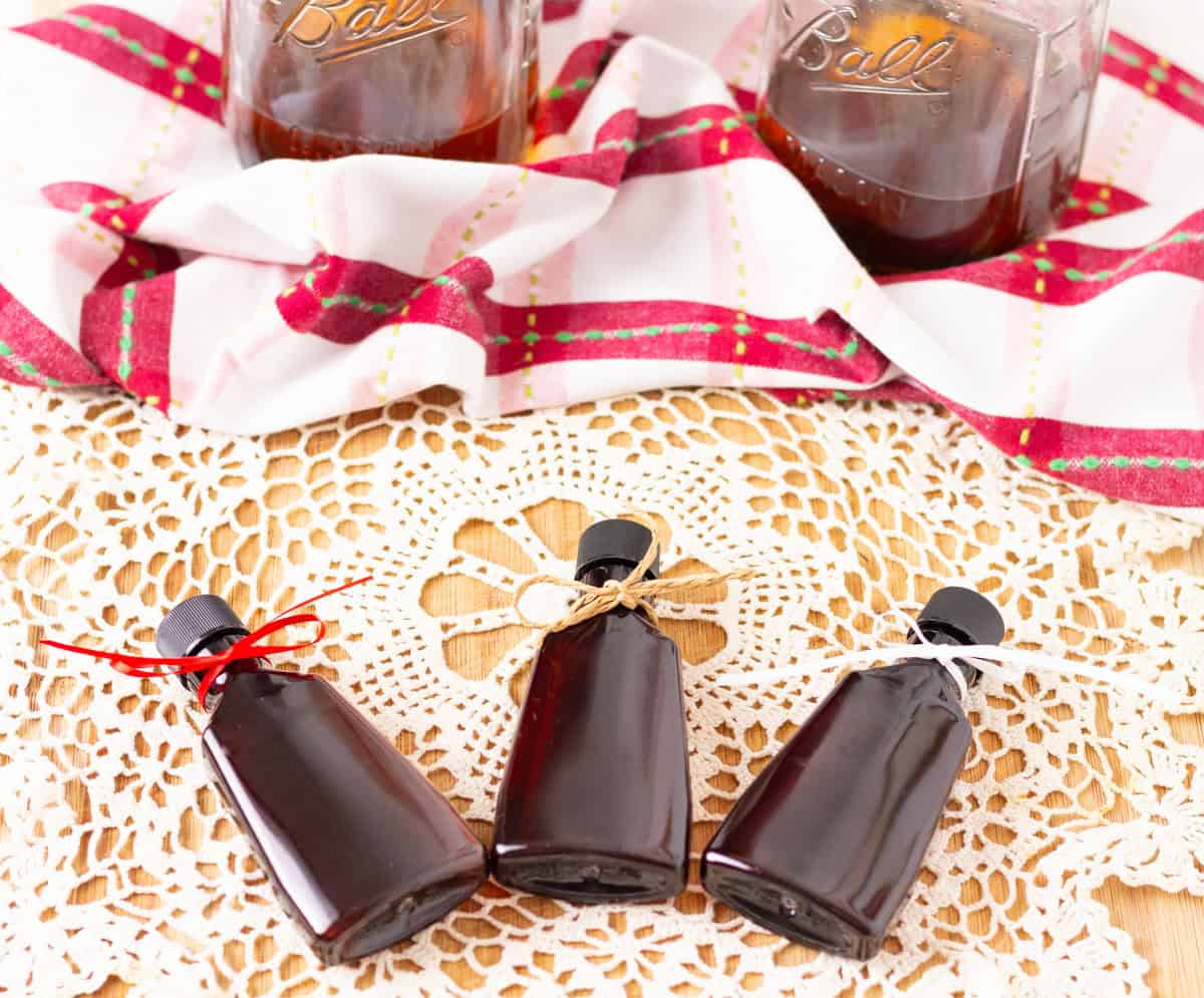 Three amber bottles of vanilla extract with ribbons of red, tan and white tied around the necks. 