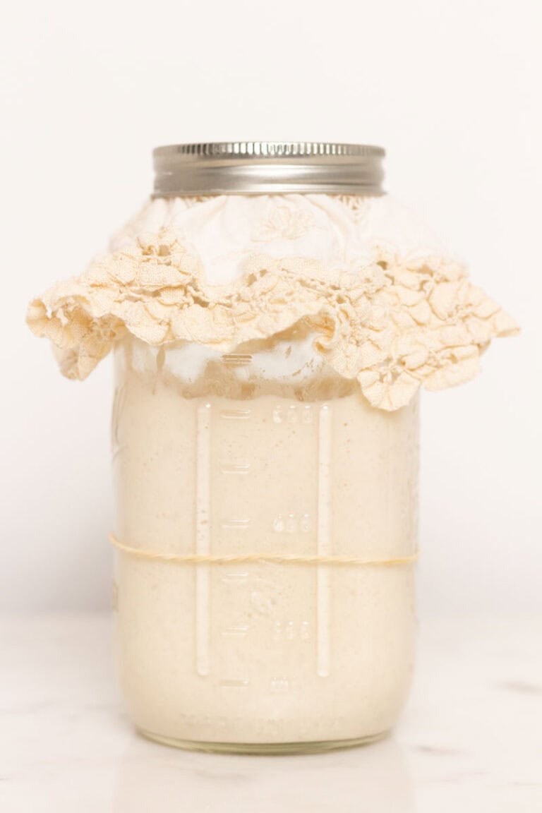 Sourdough starter in a Mason jar with a rubberband on the jar and a doily covering the jar with a lid.