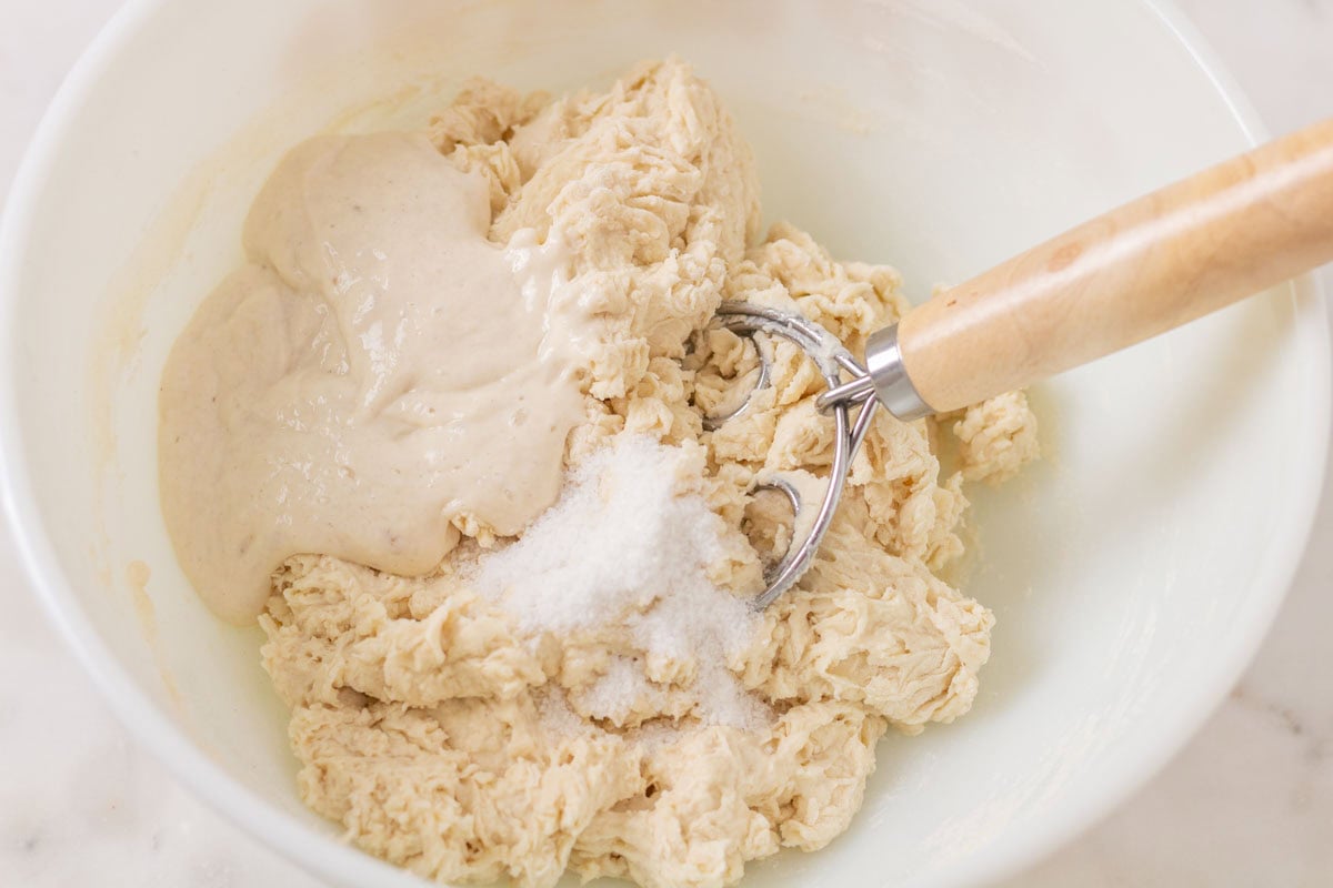 How To Make Artisan Sourdough Bread | thewendthousekitchen.com Sourdough starter and salt added to flour/water mixture. A dough whisk inside the bowl with the dough.