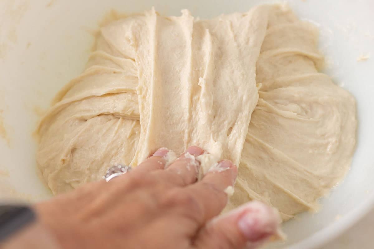 How To Make Artisan Sourdough Bread | thewendthousekitchen.com Stretching sourdough dough up and over with hands.