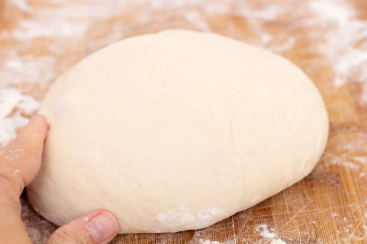 How To Make Artisan Sourdough Bread | thewendthousekitchen.com Sourdough shaped into a boule on a floured cutting board.